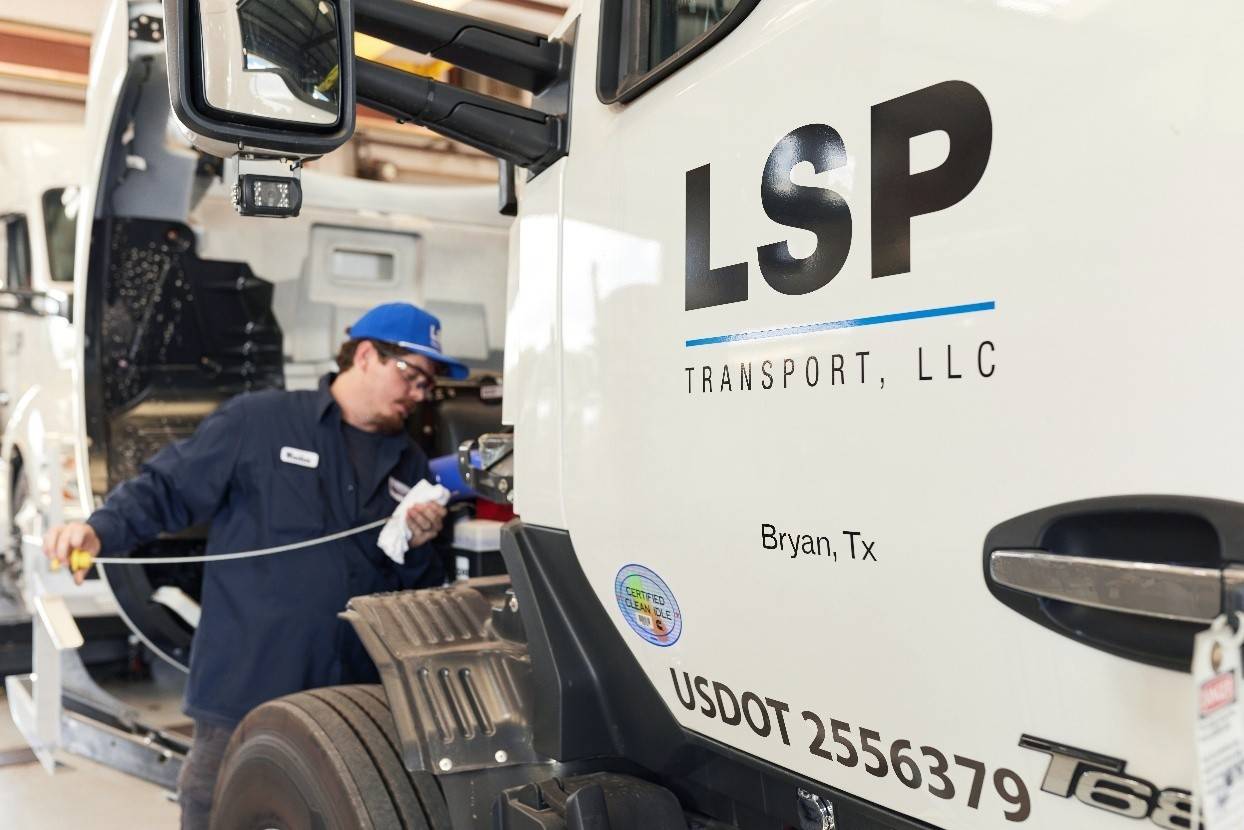 Photo of a heavy diesel engine semi-truck mechanic conducting preventative maintenance on a commercial semi-truck. The truck door has LSP Transport, LLC on the door as well as the location, Bryan, TX
